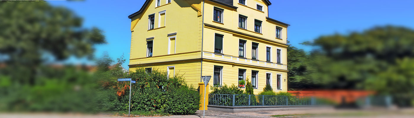 Ein gelbes mehrstöckiges Haus mit Pflanzen und einem Zaun.